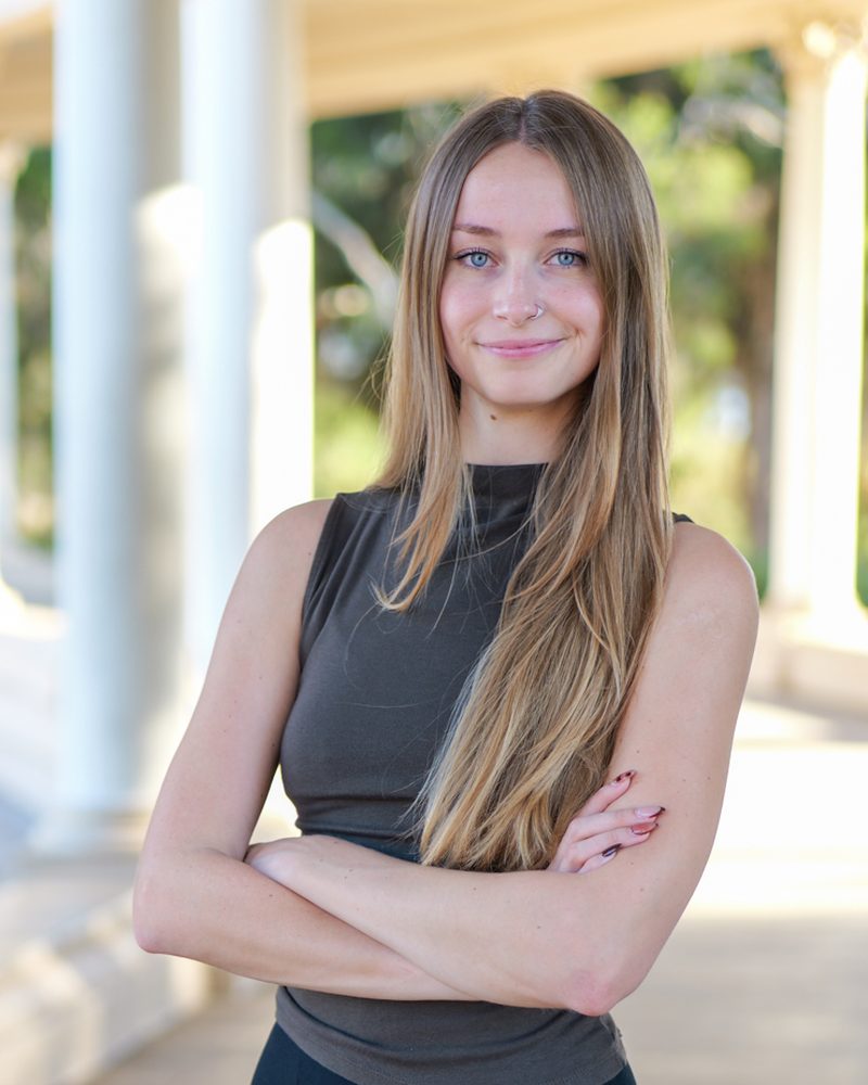 Kylie Ridge, social media and digital marketing strategist, smiling with arms crossed under a sunlit colonnade in San Diego